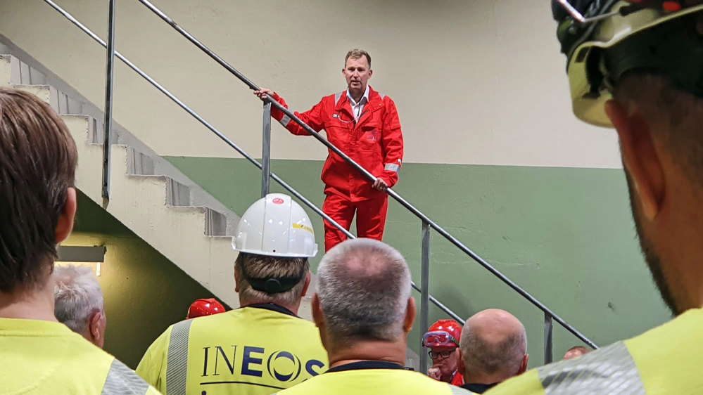 man dressed in red jacket and trousers standing in stair talking to crowd of employees