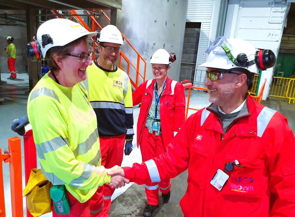 two persons shaking hands, two other persons watch and smile.