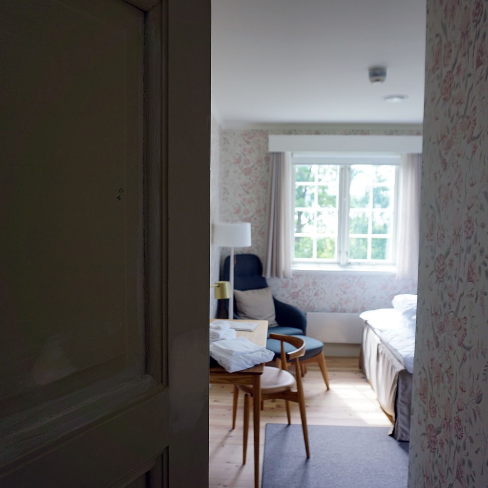 door slightly open, window, desk and chair, end of bed, blue armchair in corner of room