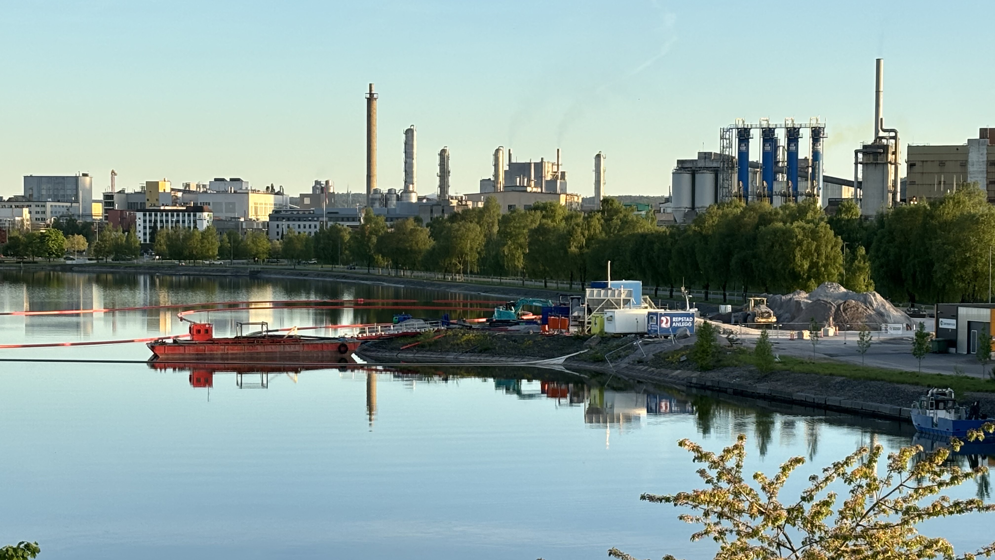 landskapsbilde, innsjø foran, anleggsområde med anleggsmaskiner, i bakgrunnen industripark