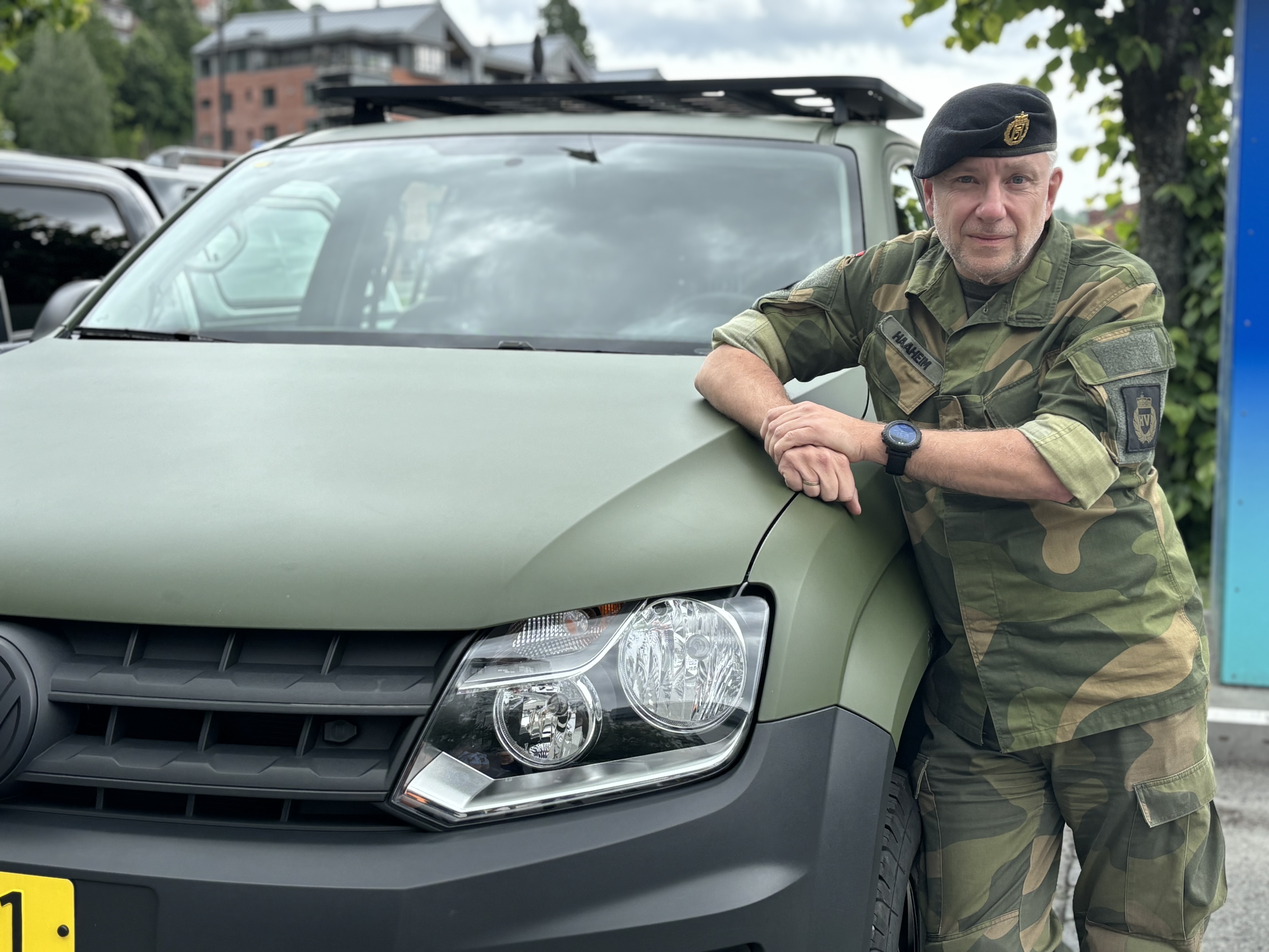 man wearing military uniform, leaning to a military vehicle, posing, sivil traffic in background