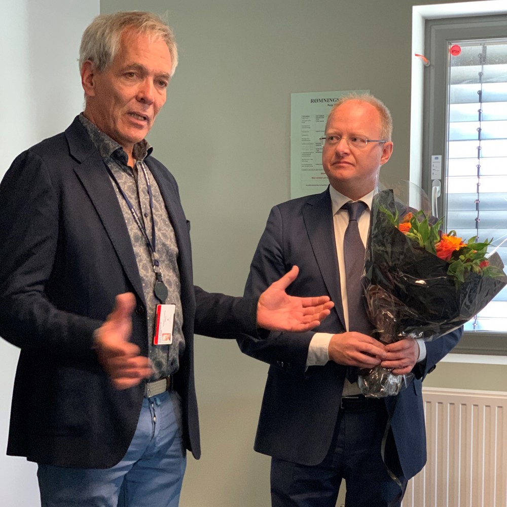 two men, suits, one holding flowers, the other making a speach and gesticulating wiht his arms. meetingroom.