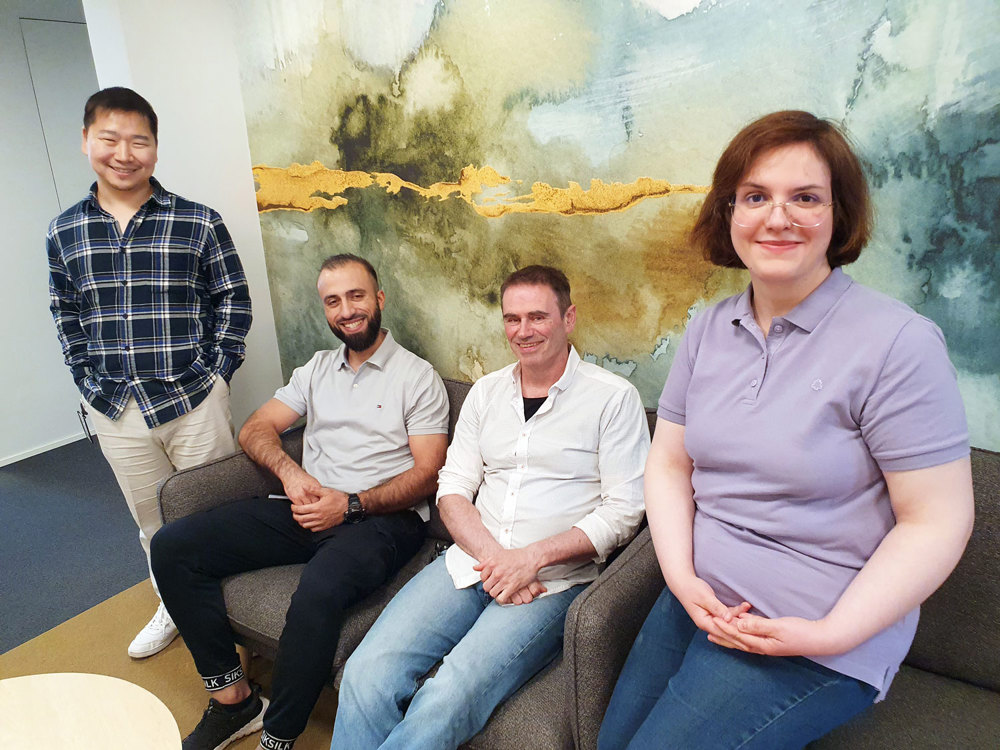 four persons standing by and sitting in a sofa. decorated wall in background. office environment.