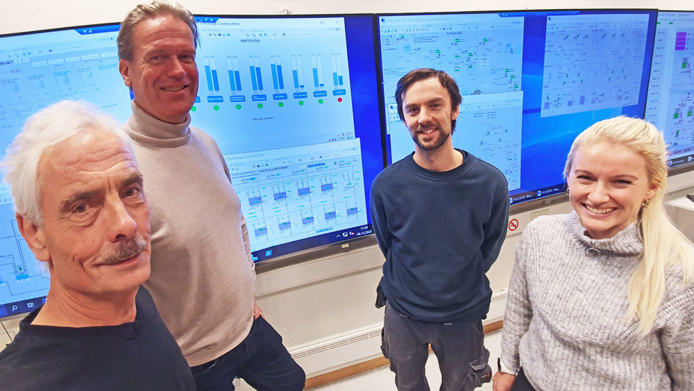 four people standing in front of monitors, posing