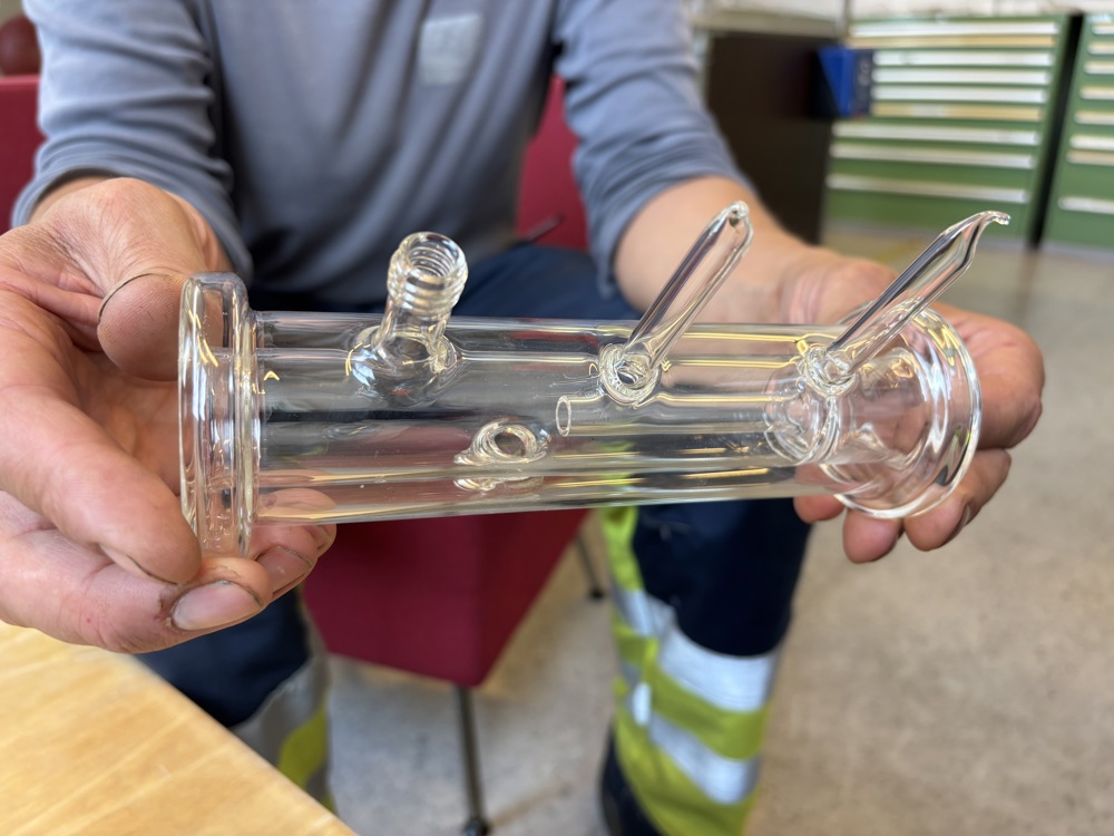 to hender som holder en modell i glassylinder med rør ut fra sylinder