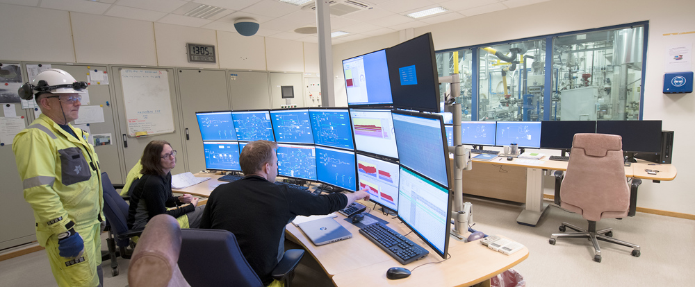 three persons in a control room with many monitors