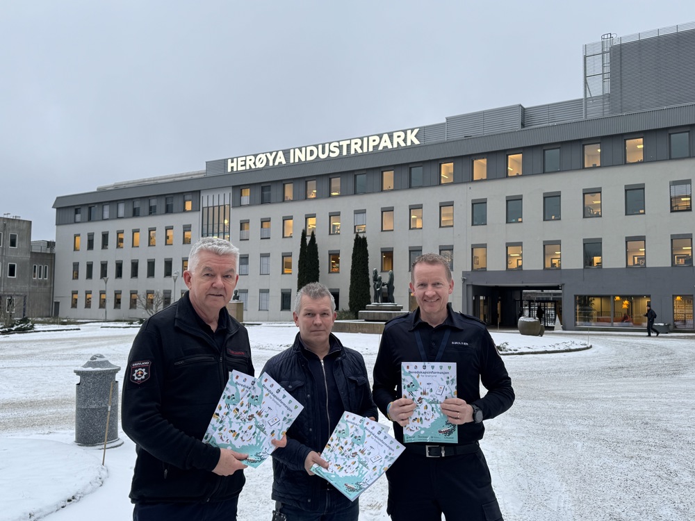tre menn som holder hver sin folder, ute, poserer, foran stort bygg med lystende bokstaver på taket