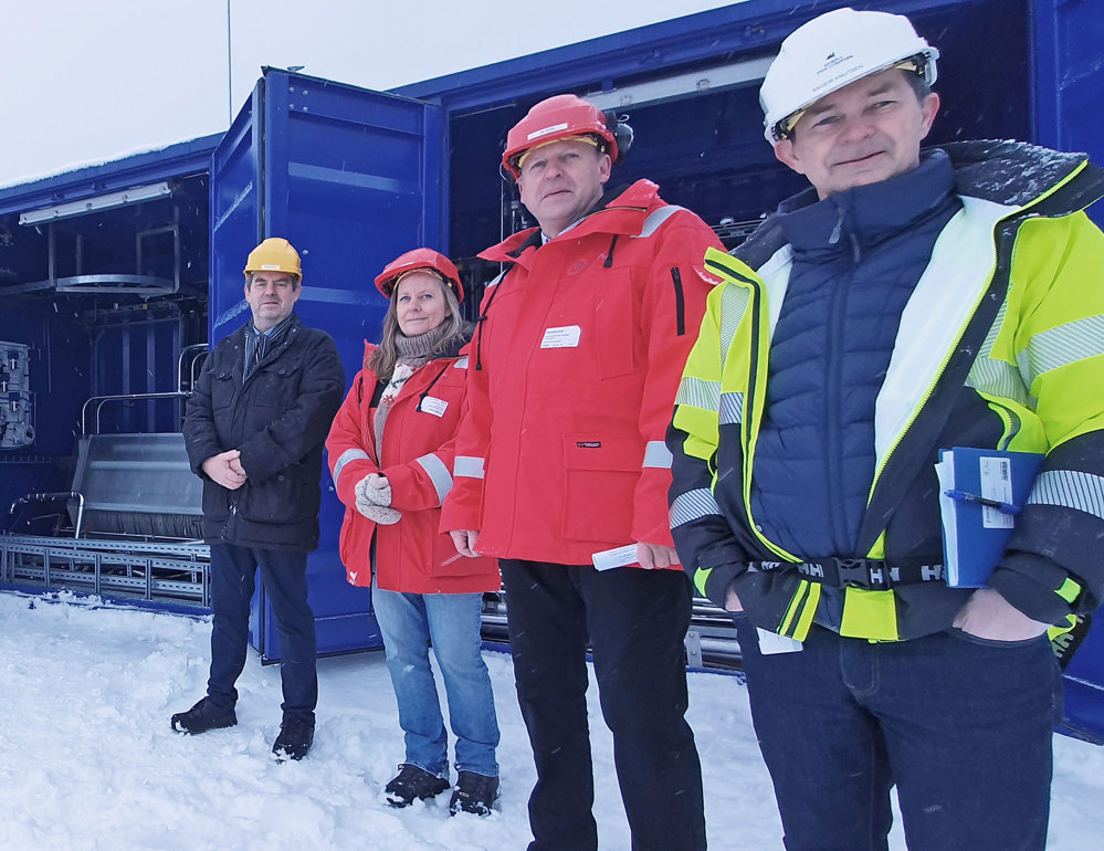 four people standing outside blue container in the snow