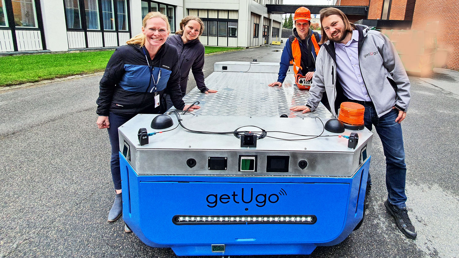 four people standing alongside robot on wheels