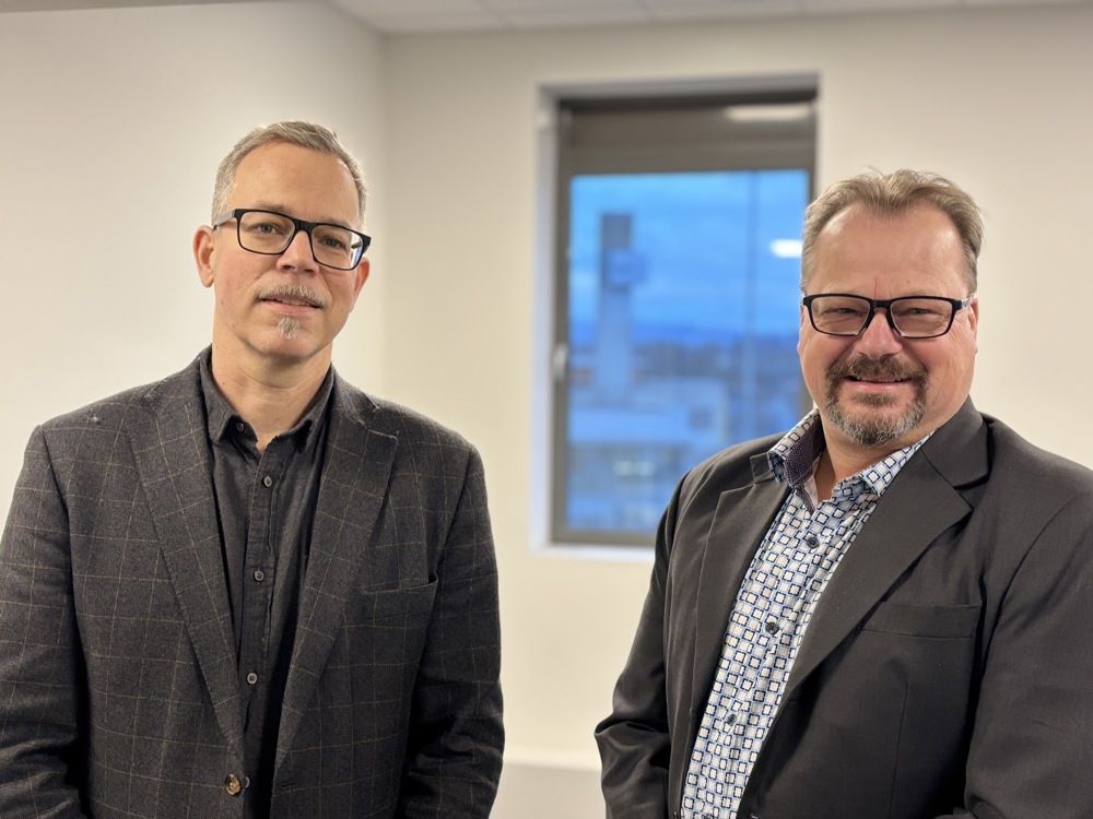 Two men, suits,glasses, posing, office corridor