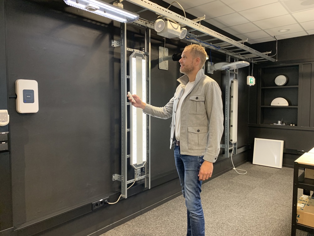 man stands in a showroom with lighting articles and a remote control