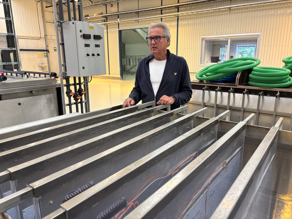 en mann står ved et anlegg med stålkammer, lange dype rom for fylling av vann og dyring av alger.
