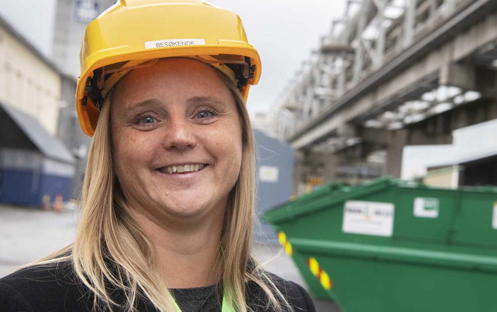 portrett av kvinne med gul besøkshjelm, ute i industripark