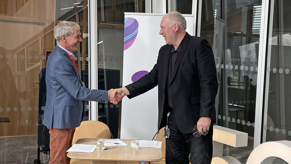 two men in suits, looking at eachother, shaking hands over an agreement