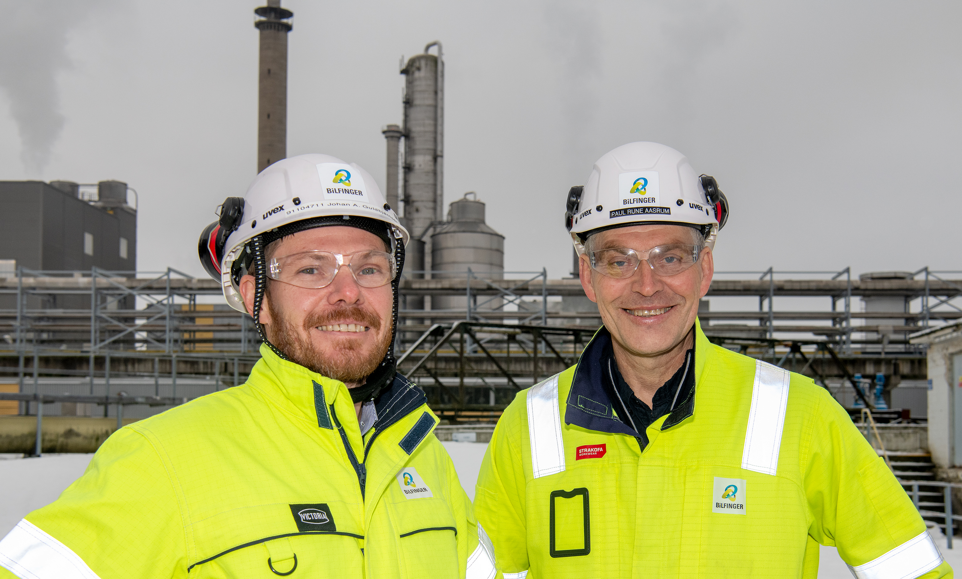 portrait, two men, yellow jackets, process industry and pipes in background