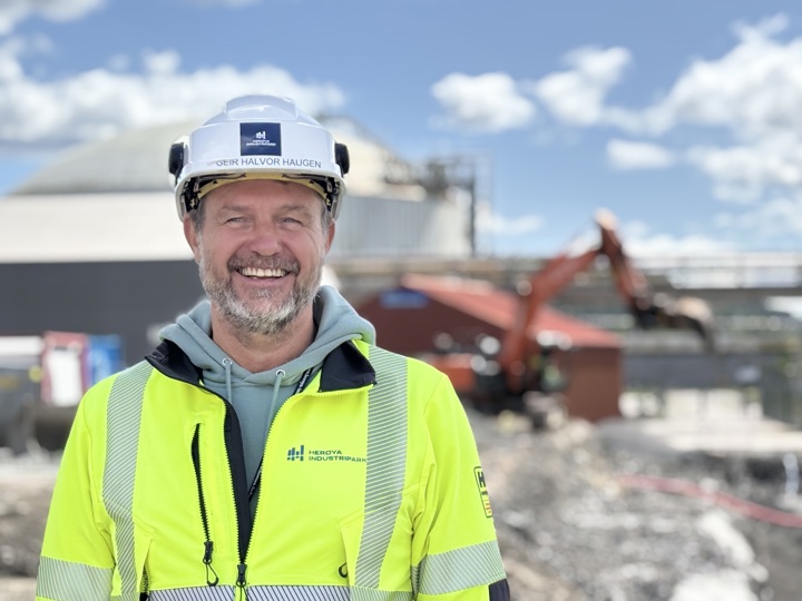 man wearing yellow jacket and white helmet, posing, standing in a construction area, industrial park