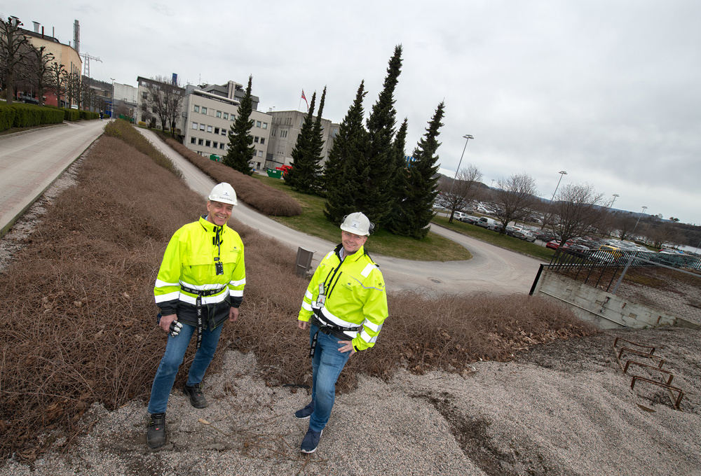 two men wearing yellow jackets and white helmets outside in industrial park