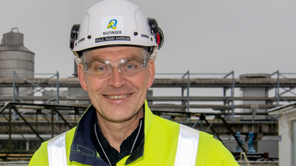 portrait of man, smiling, posing, yellow jacket, white helmet, industrial facility in background