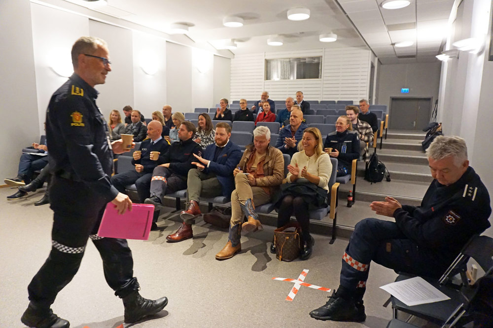 publikum i auditorium, mann i politiuniform går foran publikum