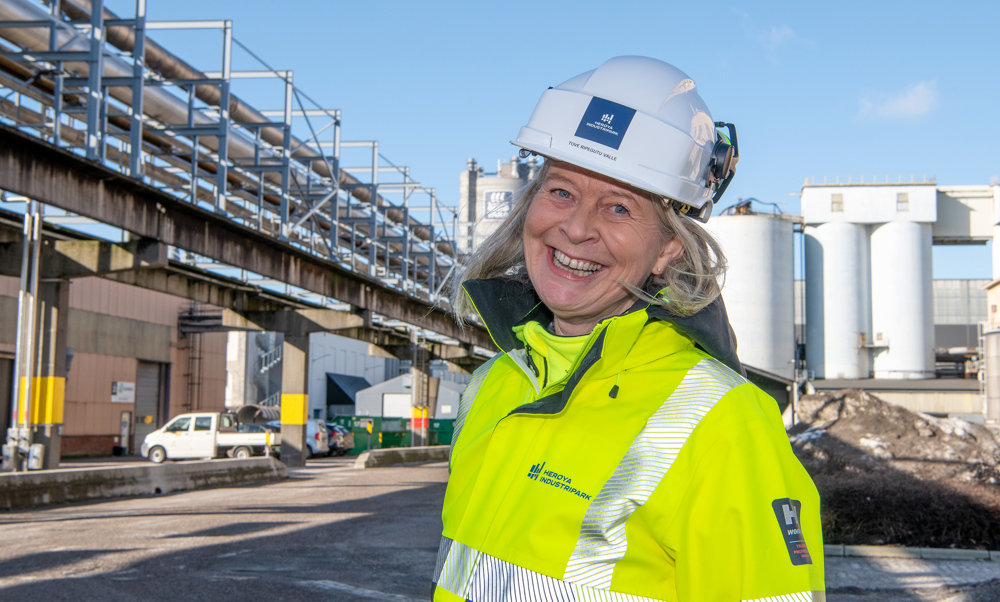 woman, posing, white helmet, yellow jacket, industry in background