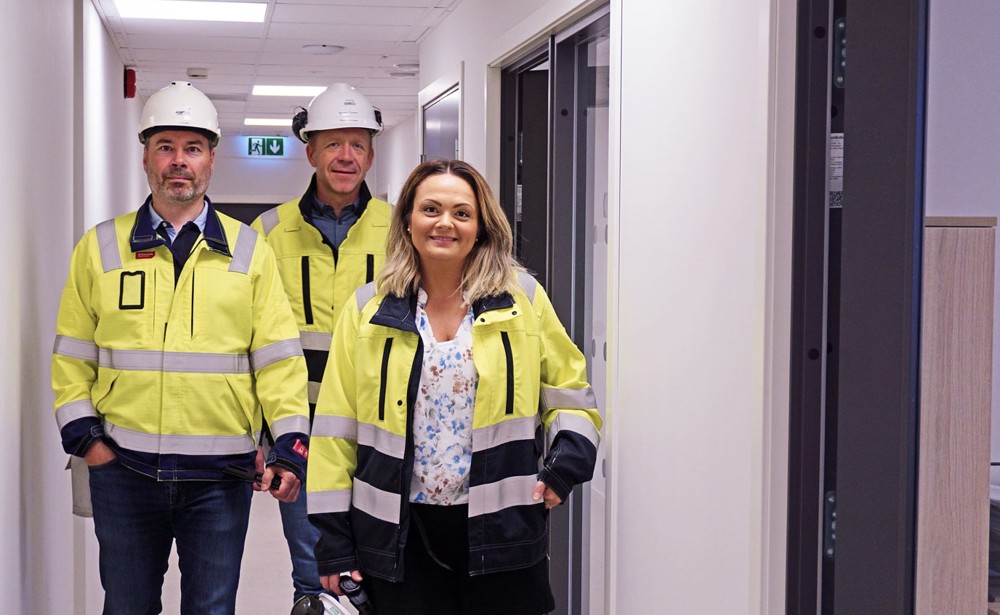 tre personer, poserer, gult arbeidstøy, går i en korridor, kontorer