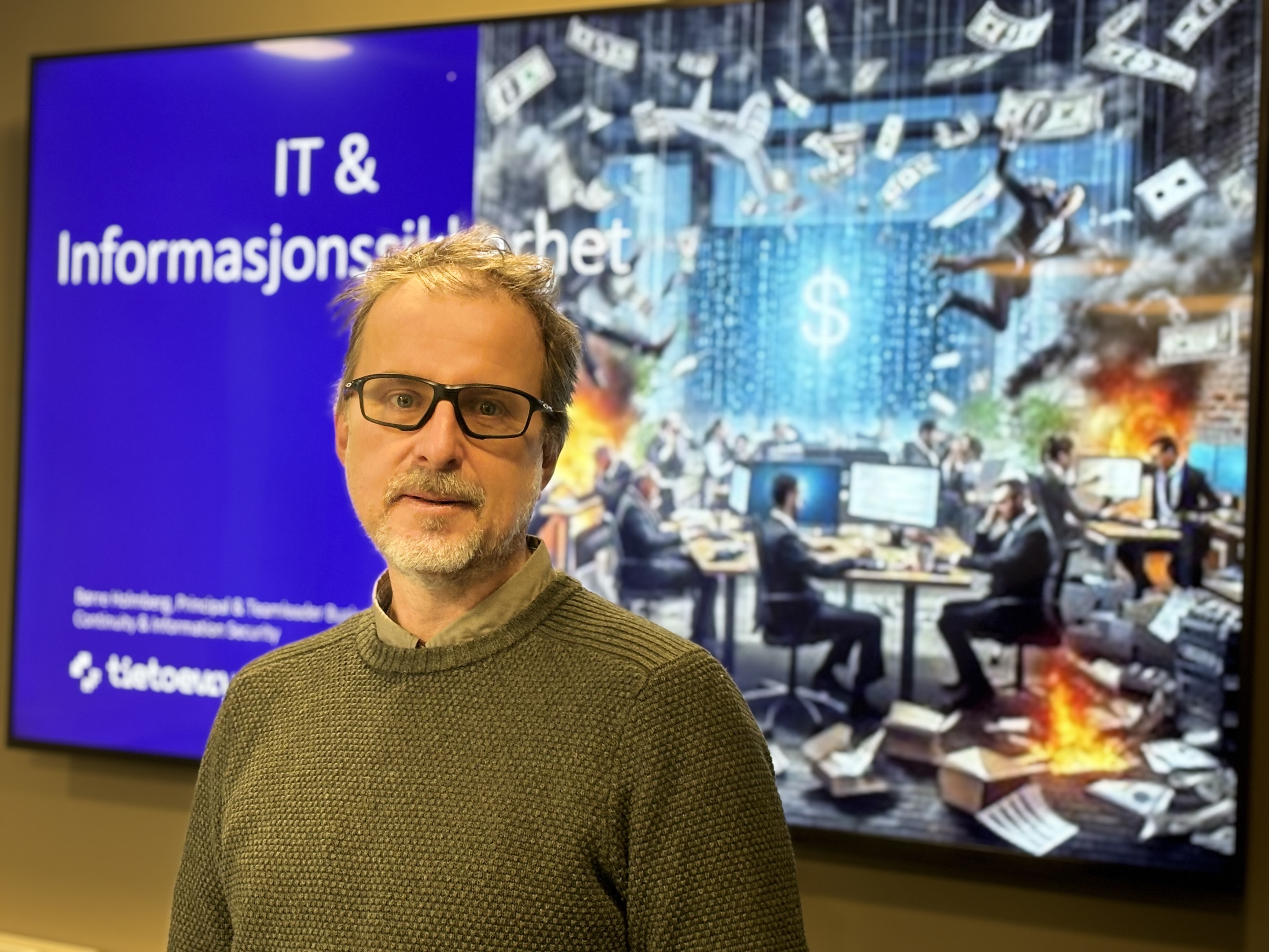 portrait of man, glasses, standing in font of screen showing chaos at office space.