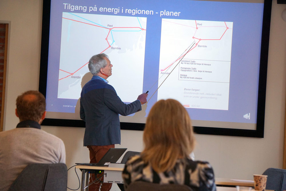 man standing in front of meeting room, pointing at presentation on screen