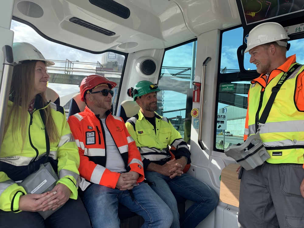 Three people sitting in seats in the mini bus, tutor standing with a steering control on his waist. All wearing personal protective equipment.