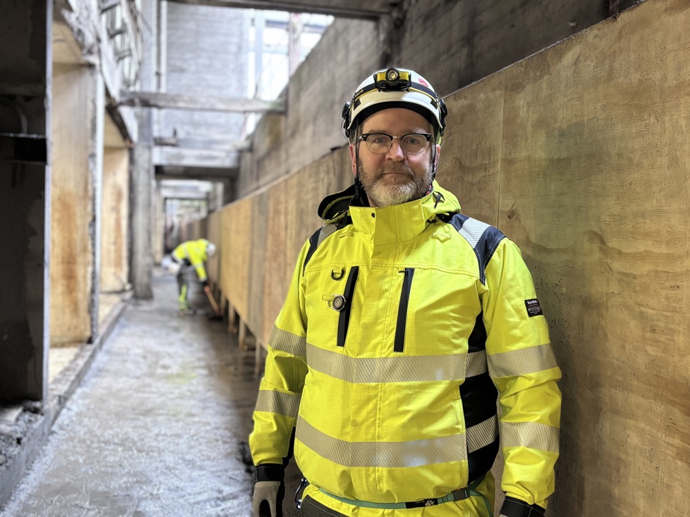 man wearing PPE, standing in basement, close to wood plates, industrial building