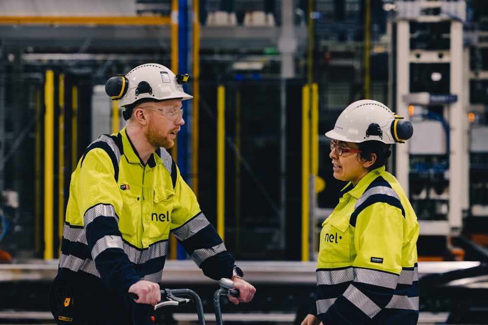 to ansatte i hvite hjelmer og gule jakker prater sammen i produksjonshall