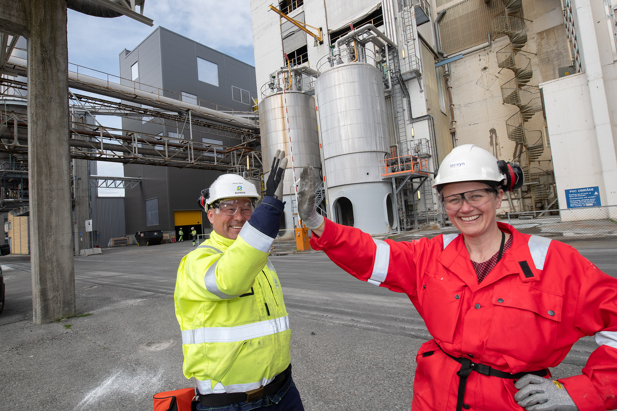 Woman dressed in red working clothes, man with yellow jacket, industrial area, high five.