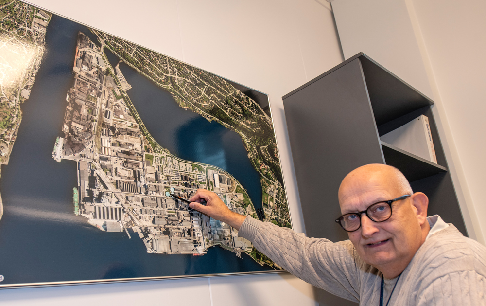 man in his office, posing, pointing on a big photo on the wall