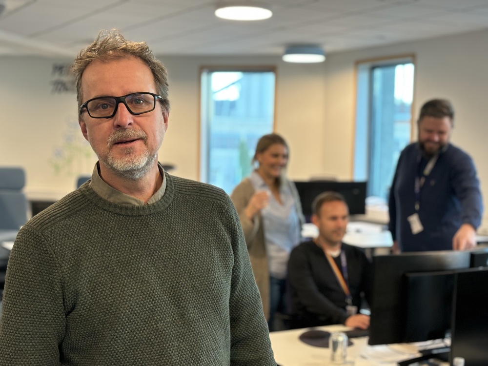 portrait of man in front, office space, colleagues in background